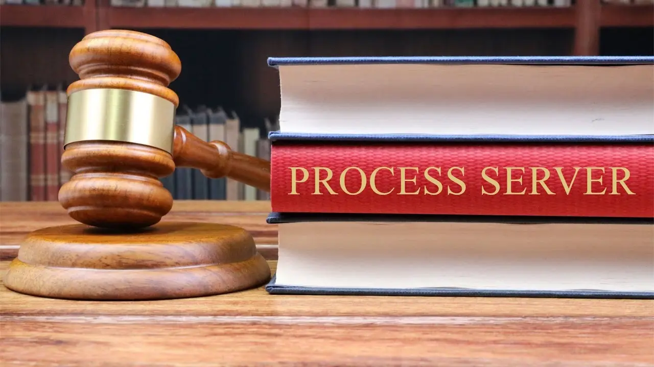 Wooden judge gavel resting on a sounding block next to a stack of law books, with 'PROCESS SERVER' printed on the red book spine.